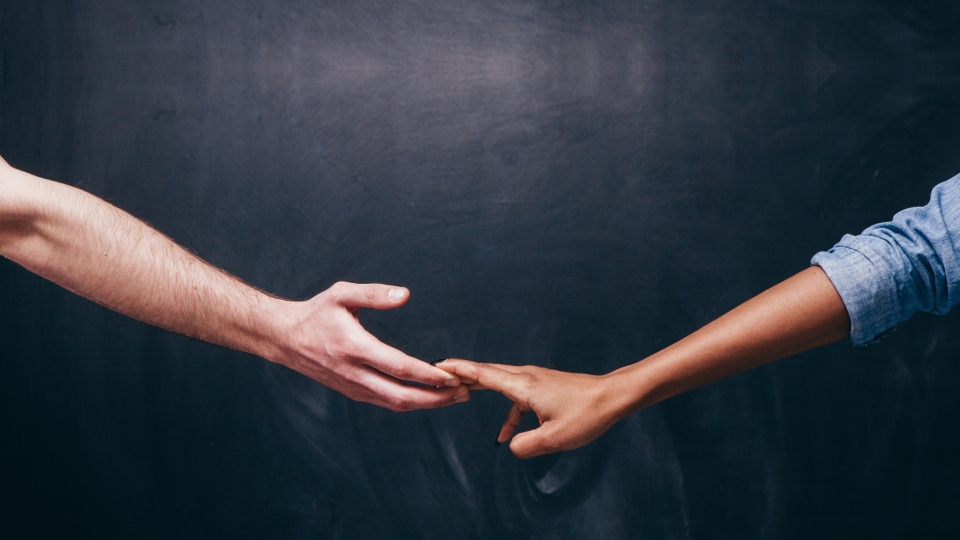 Two hands reach towards each other, almost touching, against a dark gray background.